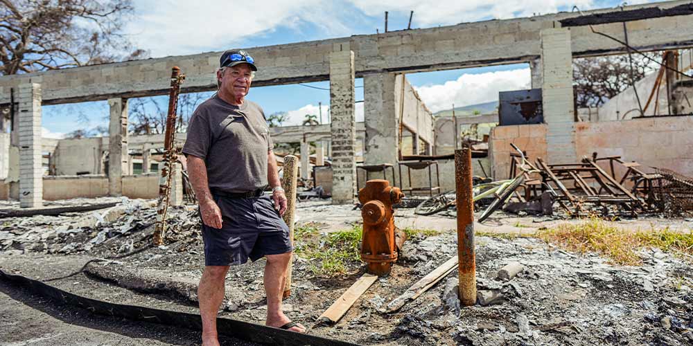 Tad Luckey stands next to the ruins of lahaina hawaii